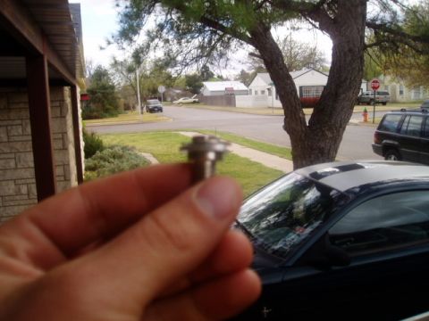 1990 Ford Bronco - Close-up of a metal fastener held in a hand, with a residential street scene behind.