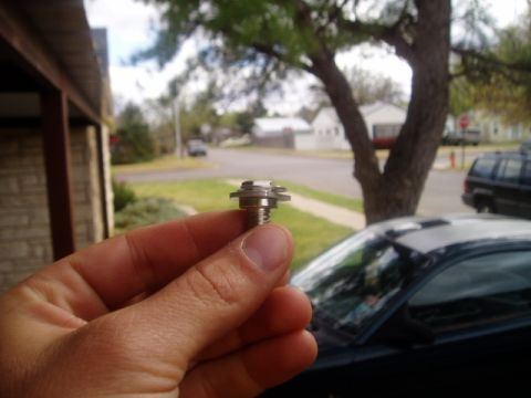 1990 Ford Bronco - A close-up of a bolt is held in front of a car and a suburban street scene.