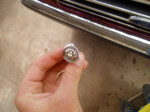 1990 Ford Bronco - A hand holds a metal header bolt with a gold-colored nut against a blurred background.