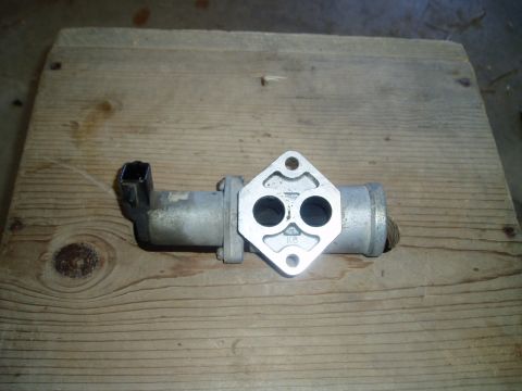 1990 Ford Bronco - An aluminum idle air control valve lies flange-up on a weathered wood board, showing its two round port openings, diamond-shaped two-bolt m…