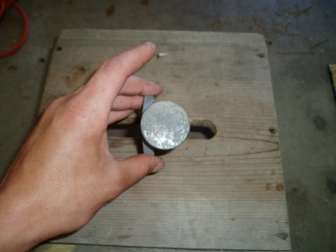 1990 Ford Bronco - A hand holds an aluminum idle air control valve end-on over a wood board, showing the round machined face of the solenoid housing and the m…