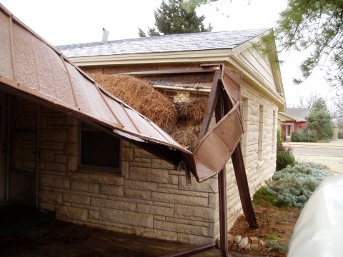1990 Ford Bronco - A carport has collapsed, spilling debris and straw onto the side of a stone-clad building.