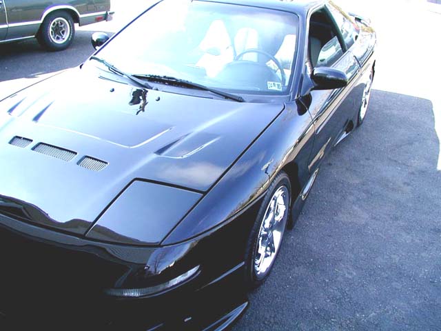 Black sports coupe with aftermarket hood vents, chrome wheels, and pop-up headlights