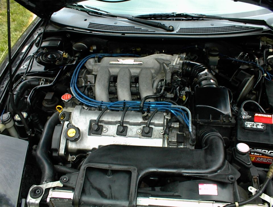 Engine bay with V6 engine, blue spark plug wires, and battery