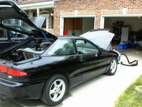 1994 Ford Probe - A black 1994 Ford Probe is parked in a driveway with its hood and trunk open, next to another vehicle.