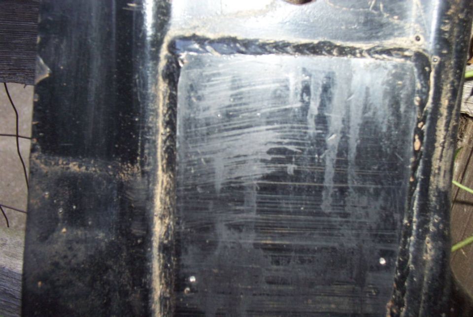 Scuffed black painted metal panel or skid plate with surface scratches outdoors