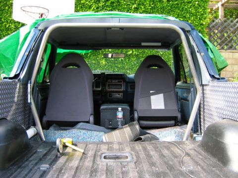 1985 Ford Bronco - The interior of a vehicle shows two bucket seats and a roll cage, with the cargo area visible.