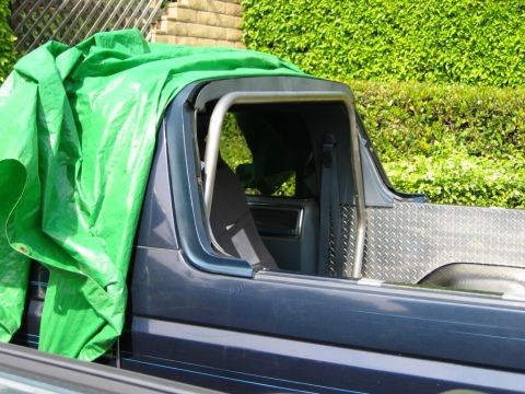 1985 Ford Bronco - The interior of a dark blue vehicle is visible, partially covered by a green tarp, with a silver roll cage installed.