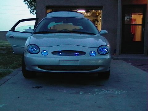 1999 Ford Taurus - Front view of a silver 1999 Ford Taurus, custom blue headlights and both front doors ajar.