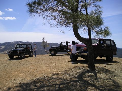 1989 Ford Bronco - Three SUVs are parked on a dusty hillside under a tree with a view of distant mountains.