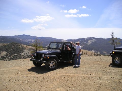 1989 Ford Bronco - Two people stand by a black Jeep Wrangler on a dirt road with a mountainous landscape behind them.