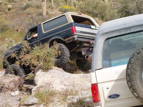 1994 Ford Bronco - A black 1994 Ford Bronco navigates a rocky trail, with another vehicle partially visible in the foreground.