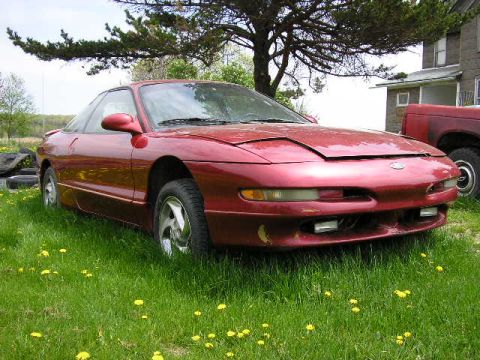 1994 Ford Probe - A red 1994 Ford Probe is parked in a grassy area with a house and another vehicle in the background.