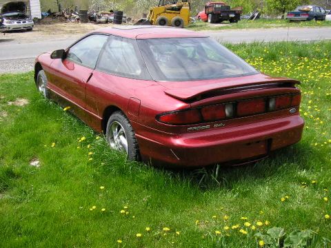 1994 Ford Probe - The rear of a red 1994 Ford Probe GT is visible, parked in a field of grass and yellow flowers.