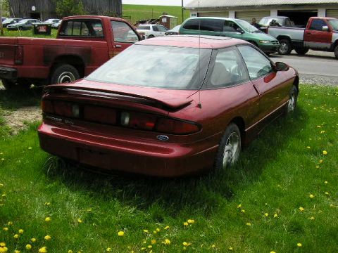 1994 Ford Probe - A red coupe is parked in a grassy area with a red pickup truck behind it.