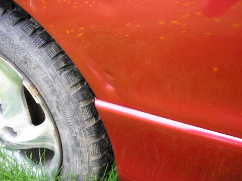 1994 Ford Probe - Close-up of a dented red car fender next to a tire, with the Supermotors.net logo in the corner.