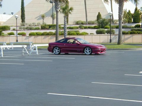 1994 Ford Probe - Maroon coupe with a sunroof open is parked in a lot with a pyramid-like building in the background.