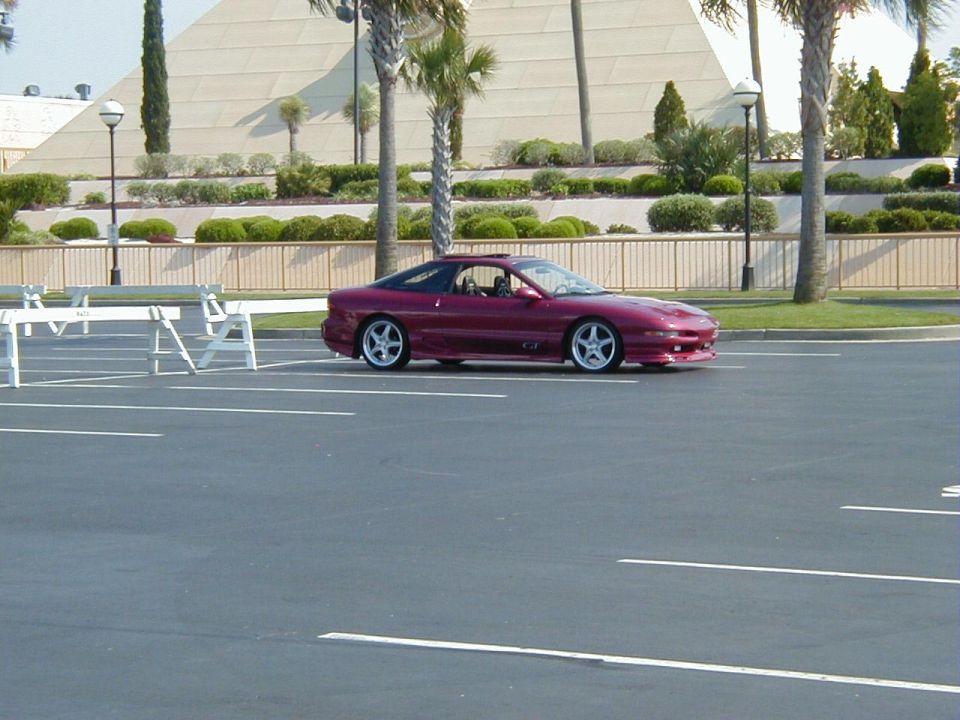 Maroon coupe parked in a lot, side view with front quarter visible. Sunroof open, aftermarket wheels