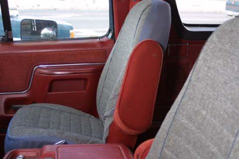 1989 Ford Bronco - Interior view of a car with red door panels and patterned seats, showing a side mirror.