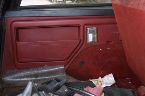 1989 Ford Bronco - The interior of a vehicle shows a red door panel and carpeted rear cargo area with some items on the floor.