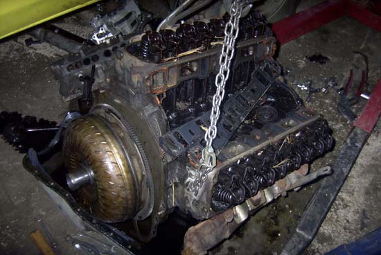 Disassembled greasy V8 short block with exposed valvetrain, lift chain and torque converter