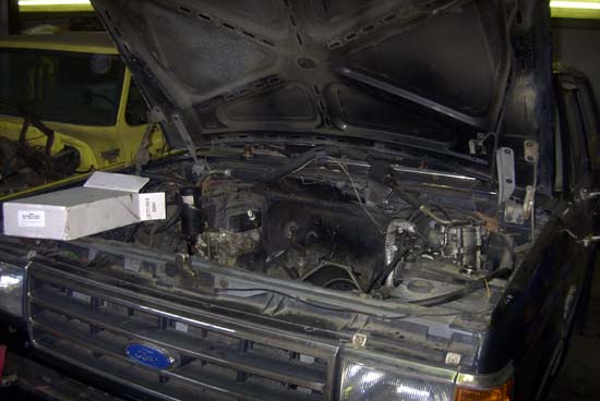 Stripped engine bay of a blue 1980s Ford truck with radiator removed in a shop