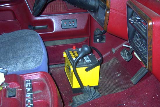 Truck cab interior with red carpet, yellow battery mounted on floor and woodgrain dash trim