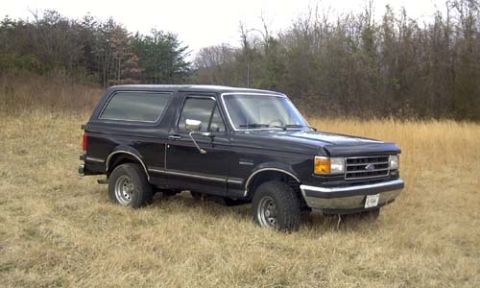 1989 Ford Bronco - Passenger-side three-quarter front view of a black full-size Ford Bronco with a removable hardtop, black fender flares, chrome bumper and g…