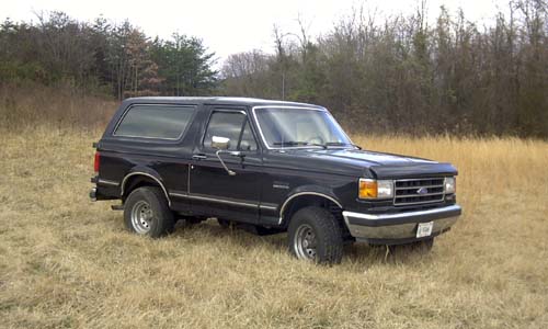 Black full-size Ford Bronco parked in dry winter field, 3/4 front passenger-side view