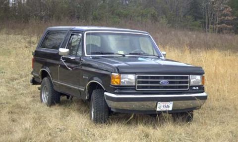 1989 Ford Bronco - Three-quarter front view of a black late-1980s Ford Bronco with a removable hardtop, chrome grille and bumpers, chrome tow mirrors and a '4…