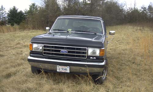 Front view of a black late-1980s Ford Bronco 4x4 parked in tall dry grass