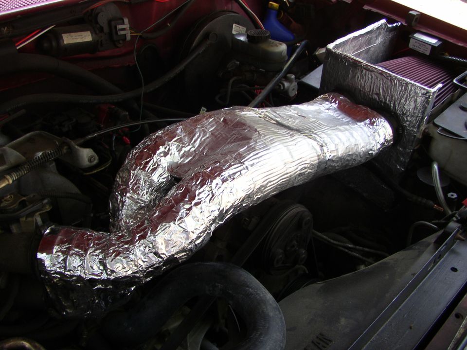 Engine bay with silver-wrapped intake tube and red air filter. Some hoses and belts are visible