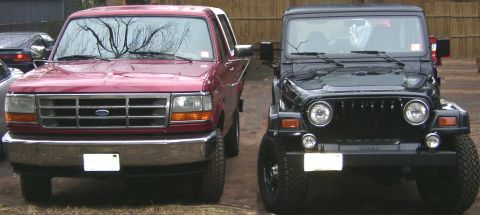 1995 Ford Bronco - A 1995 Ford Bronco is parked next to a black Jeep Wrangler, both facing forward.