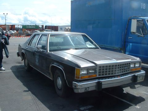 1999 Ford Crown Victoria - A dark sedan, possibly a Ford Crown Victoria, with a distinctive grille and bumper marking '82'.