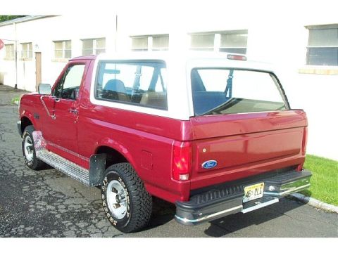 1995 Ford Bronco - This red Ford Bronco with a white top is parked outside a building. The license plate is visible.