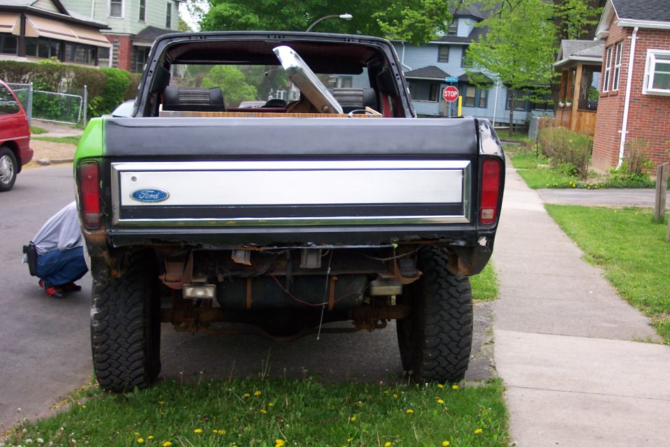 Rear of a lifted Ford truck with chrome Ford tailgate and open cab, parked on sidewalk