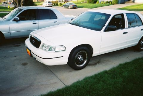2000 Ford Crown Victoria - Two sedans parked on a driveway, one white Ford Crown Victoria and a silver car.