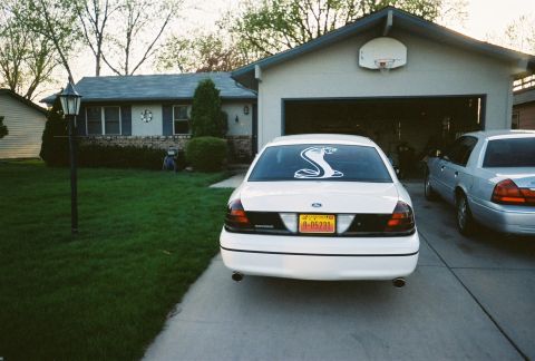 2000 Ford Crown Victoria - Two Ford Crown Victorias are parked in a driveway in front of a suburban house.