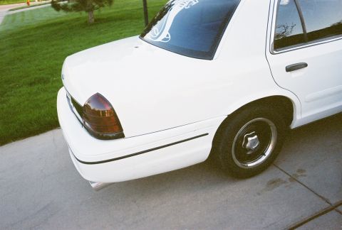 2000 Ford Crown Victoria - A white sedan is parked on a concrete driveway next to a grassy lawn.
