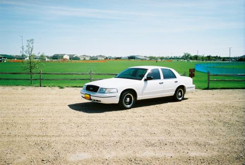 2000 Ford Crown Victoria - White 2000 Ford Crown Victoria parked on gravel lot under a clear blue sky.