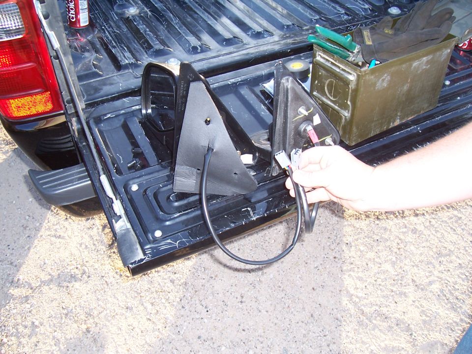 Black truck bed with two side mirrors, one held by a hand, and a green ammo can with tools