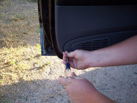 2003 Ford Ranger - A person is removing a car door panel with a screwdriver.