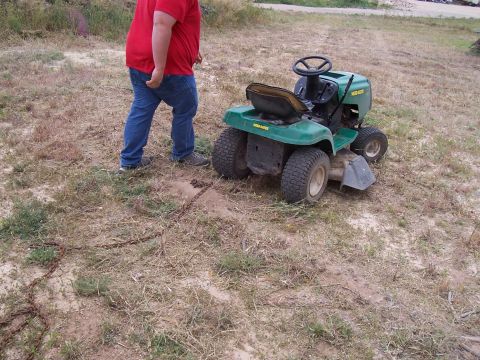 2003 Ford Ranger - A person is pulling a green riding lawn mower with a chain across a dry, grassy field.