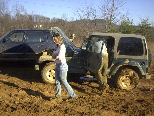 Green Jeep Wrangler with hood up stuck in mud beside a blue Ford Explorer