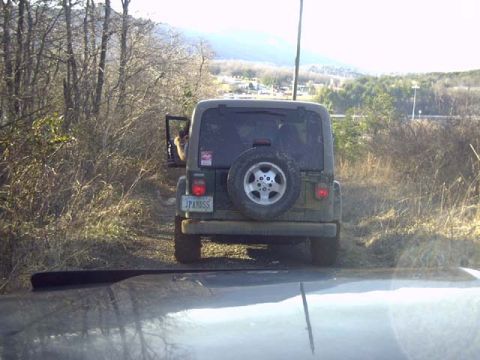 1989 Ford Bronco - Rear view of a mud-splattered green Jeep Wrangler with a hardtop, swing-away spare on an alloy wheel and a vanity plate reading JPANDSS, st…