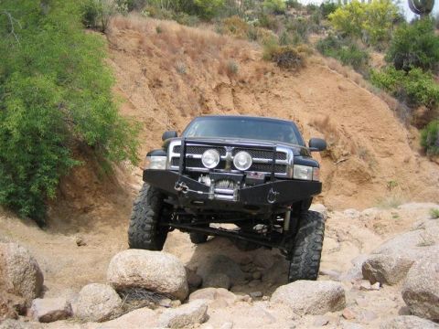 1994 Ford Bronco - Modified pickup truck driving over rocks on an off-road trail.