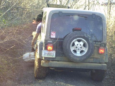 1989 Ford Bronco - Rear view of a mud-covered white Jeep Wrangler on a brushy trail, with a swing-away spare carrying a Goodyear tire on an alloy wheel, Virgi…