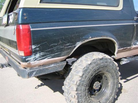 1994 Ford Bronco - This Ford Bronco shows significant body damage and rust, with a large off-road tire visible.