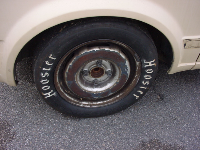 Close-up of a Hoosier tire on a rusty wheel. Car body is visible in the background