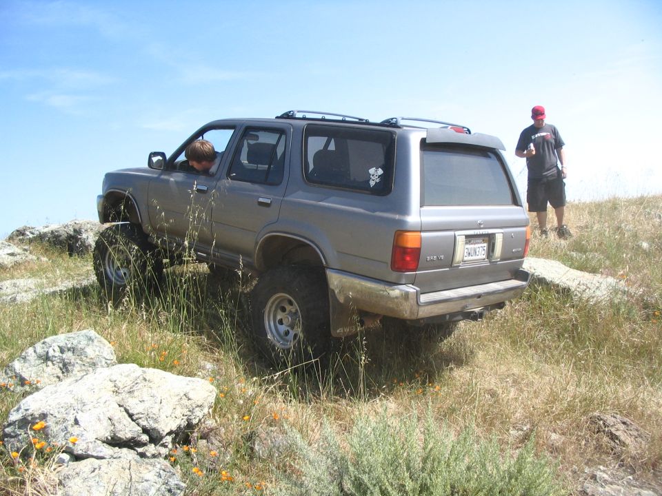 Rear of gray lifted Toyota 4Runner parked on grassy ridge, two men standing beside it